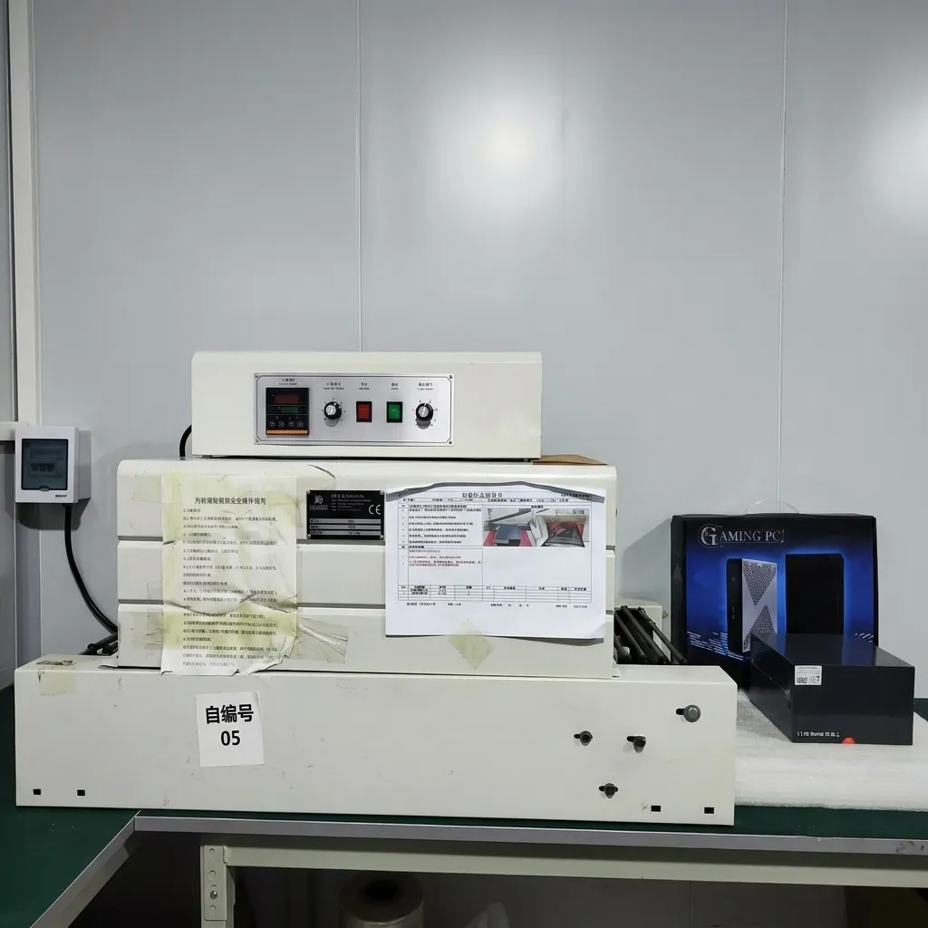 A heat shrink packaging machine on a green workbench in a clean laboratory setting, with a Gaming PC box resting next to it.