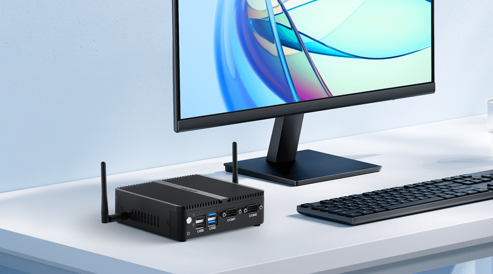A black Hystou H3 industrial mini PC with dual Wi-Fi antennas, USB ports, and COM1/COM2 serial ports on a white desk, connected to a modern monitor and keyboard.